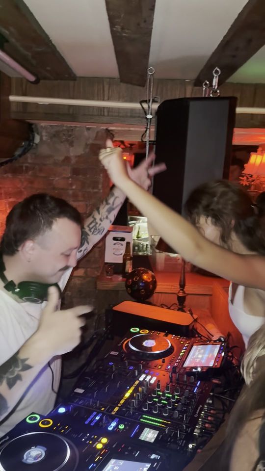 A woman reaches across the booth toward DapSoul at the decks